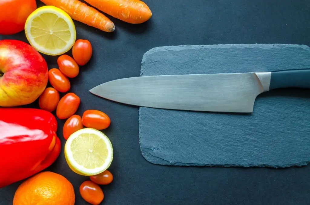 sharp Japanese knife on cutting board next to fruits and vegetables