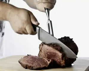 man's hands using knife and fork to cut prime rib