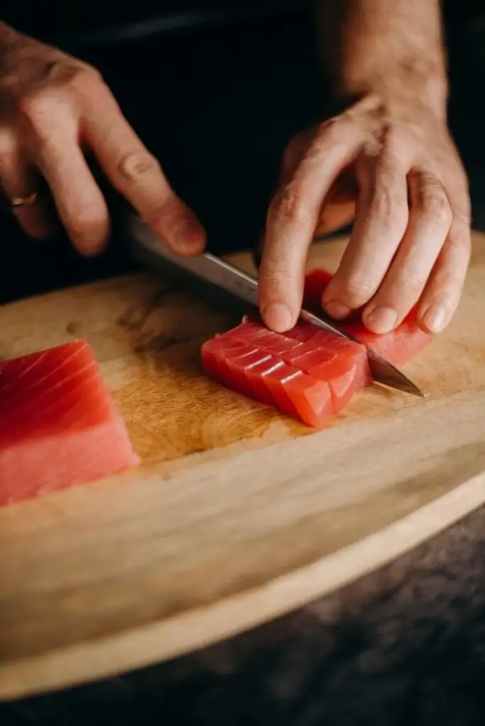 hands with knife cutting salmon on cutting board