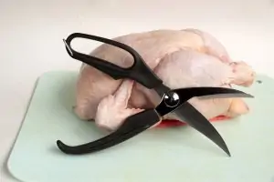 black kitchen shears in front of raw chicken on white background