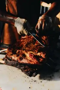 person with gloves using huge knife to cut into cooked meat