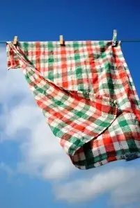 white red and green checked kitchen towel hanging on clothes line with blue sky over it