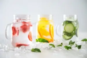 three mason jars of infused water on ice and mint leaves with white background