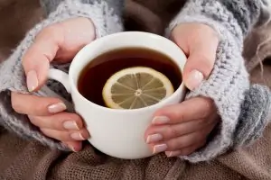 woman's hands holding white mug of tea with lemon slice
