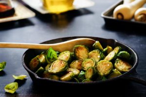brussel sprouts and wooden spoon in cast iron skillet on black table