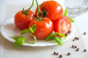 stemmed tomatoes on white plate with a few black peppercorns on white table