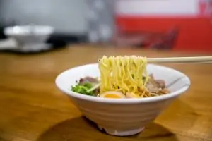 white bowl of ramen and vegetables and boiled egg on table