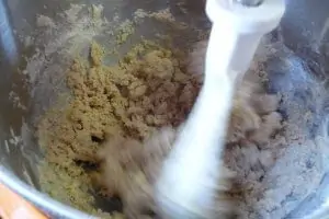 Inside of a KitchenAid mixer bowl with whirring white paddle beating a mixture of brown sugar and eggs