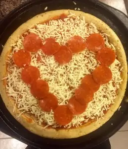 high quality pepperoni in the shape of a heart on an uncooked pizza surrounded by shredded mozzarella cheese