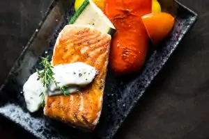 cooked fish on a black plate with vegetables and white sauce
