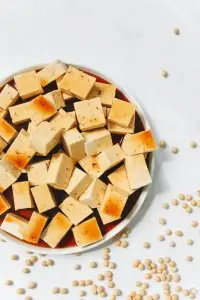 a white bowl of cubed grilled tofu with small beans scattered around it