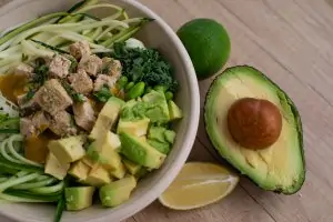 healthy salad with tofu on top in white bowl with half an avocado and lemon slice beside bowl
