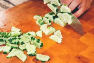 cucumber being sliced and diced on cutting board with knife