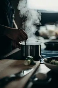person's hand using utensil to stir steaming food in cuisinart multiclad pro pot on stove