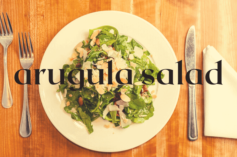 white bowl on wood table with arugula salad