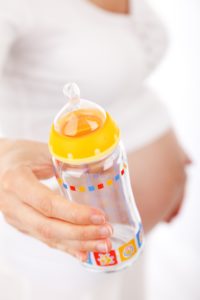 pregnant woman holding clear baby bottle with yellow cap