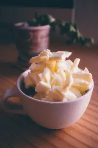 white coffee cup filled with pats of butter on wooden surface
