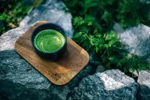 black cup of green tea on wooden cutting board on rock with greenery