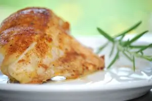 cooked chicken breast on white plate with rosemary sprig