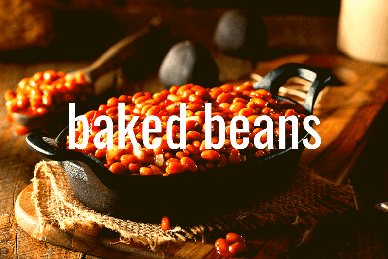 baked beans in cast iron casserole dish on wooden table with kitchen implements in background
