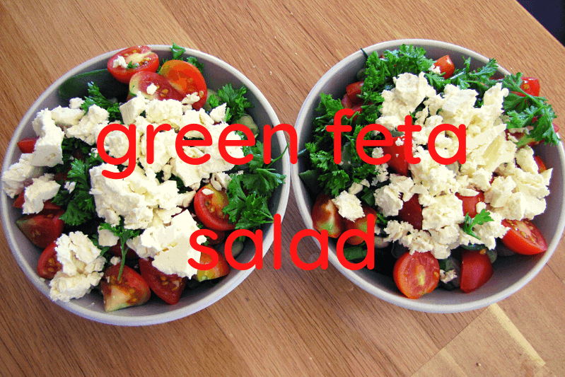 two bowls of green salad with feta on wooden table