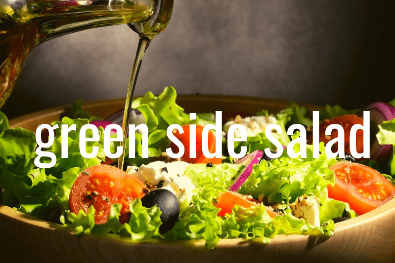 bottle of oil drizzling over green salad in wooden bowl with gray background