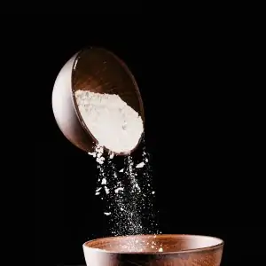 wooden bowl of powdered sugar being poured into another wooden bowl with black background