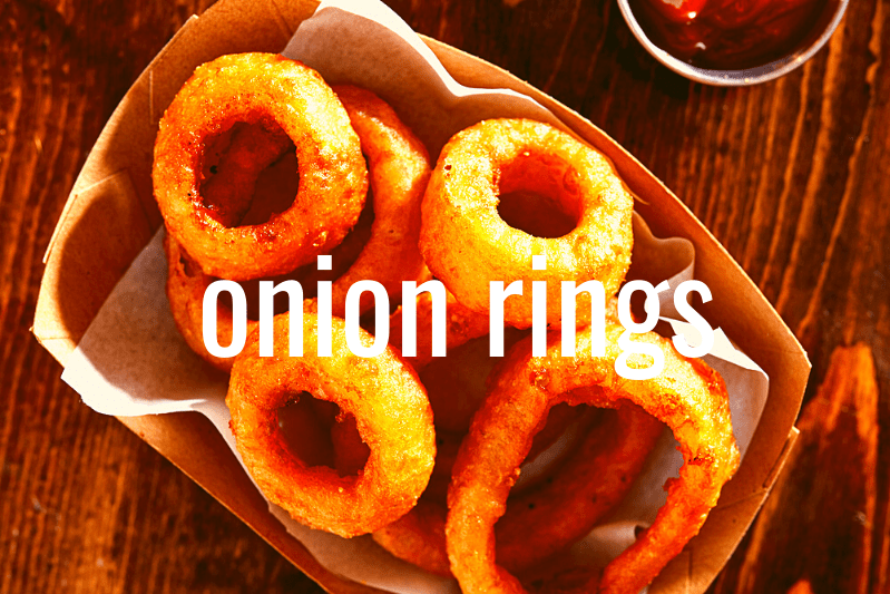onion rings in basket on wooden table with metal ramekin of ketchup