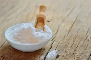 white bowl of baking soda with wooden scoop on wooden table