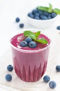 blueberry and granola smoothie in glass tumbler on wood surface with blueberries strewn about