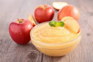 small glass bowl of applesauce on wooden table with apples