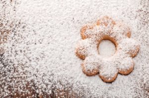 flower shaped cookie on wooden table surrounded by sprinkled powdered sugar