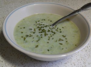 white bowl of asparagus soup and spoon on granite surface