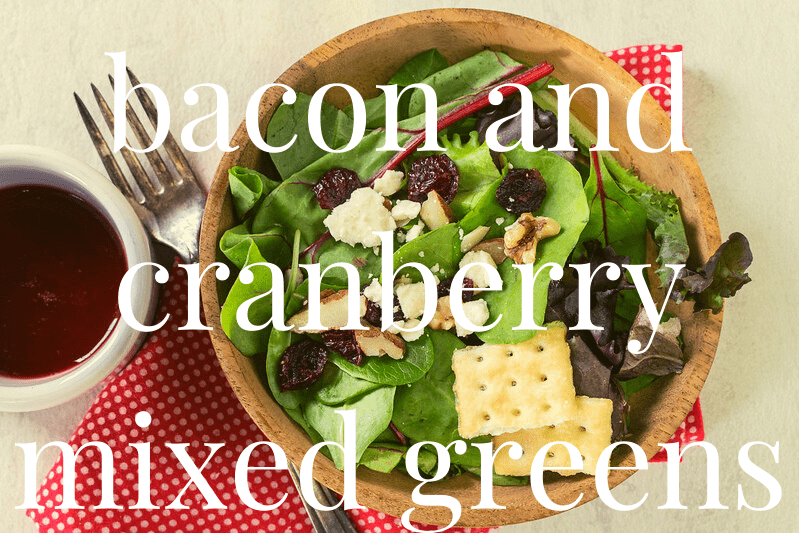 cranberry and arugula salad in wood bowl on white table with fork and red napkin