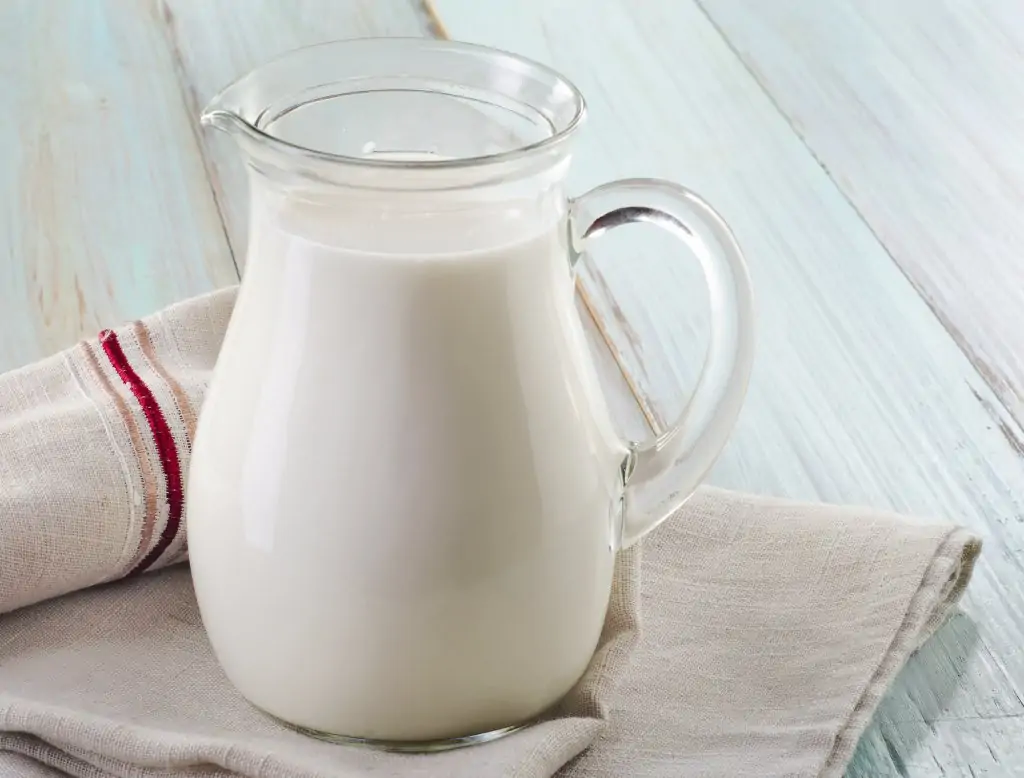 glass pitcher of milk on white wooden table with dishcloths