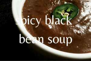 close up of black bean soup in white bowl with slice of jalapeno on top
