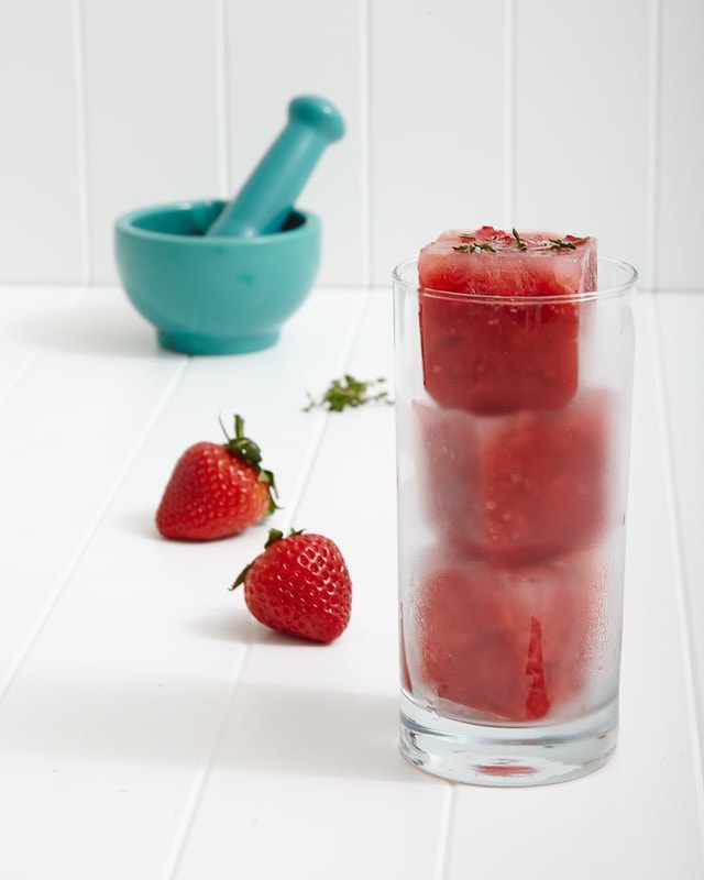 blue mortar and pestle and two strawberries in background of glass filled with frozen strawberry drink with white background