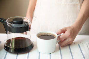Barista hand holding cup of coffee and jug on striped placemat at home