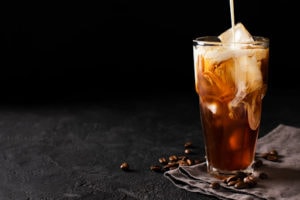 tall glass cold brew coffee with ice and milk on black or dark background