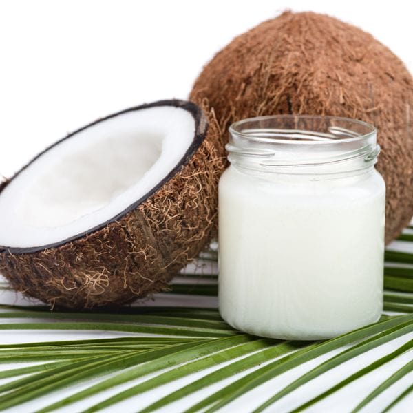organic coconut oil next to a halved coconut on a palm leaf