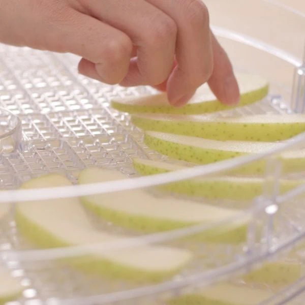 someone putting green apple pieces into a dehydrator
