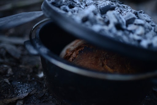 Closeup of bread in cast iron pot with fire coals on the cover