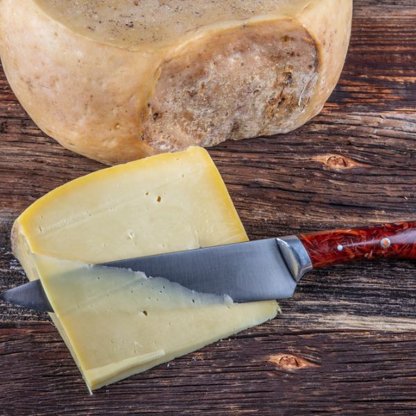 Gruyere Cheese sliced with a knife on a wooden surface