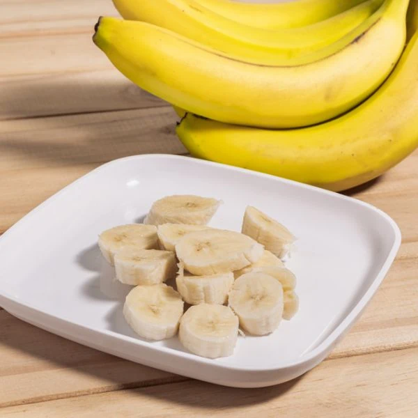 sliced bananas in a white plate next to a bunch