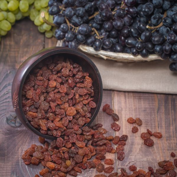 a bowl of raisins on wood with green and purple grapes