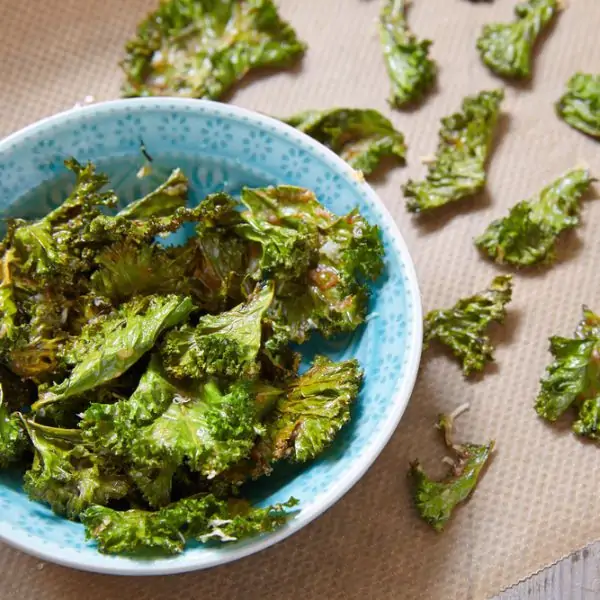 kale chips in a blue bowl and spread out on parchment paper
