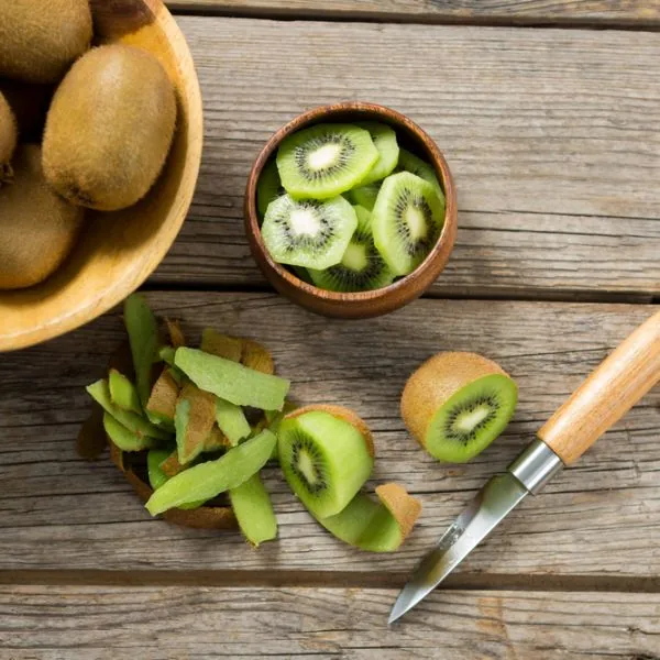 kiwi being peeled and sliced into a wooden bowl