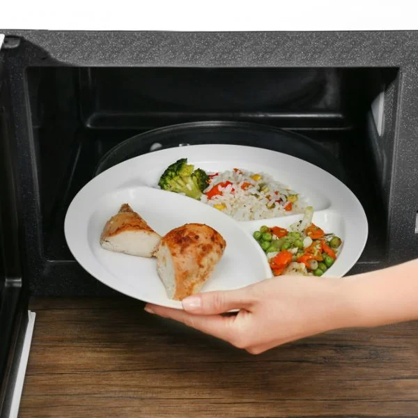 Someone putting a rice meal with veggies and chicken into a white microwave