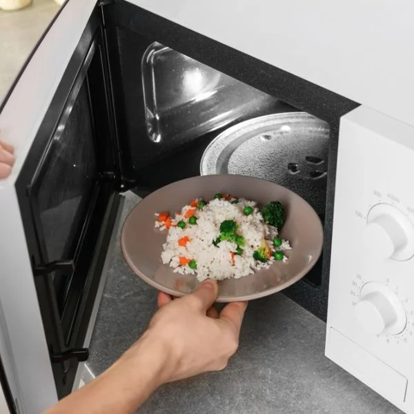 Someone putting rice and veggies into a white microwave