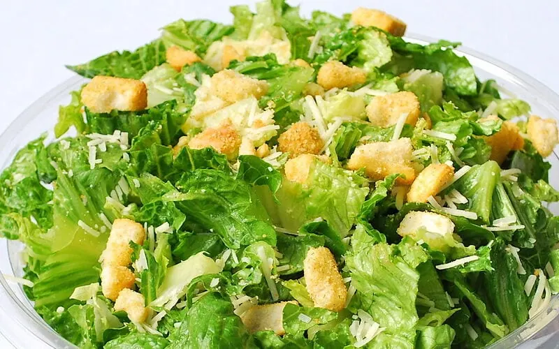 Green salad with dressing in a clear bowl on a white table